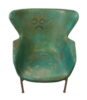 Front view of a multicolored fiberglass chair with a simple drawn face on the backrest and thin steel legs.