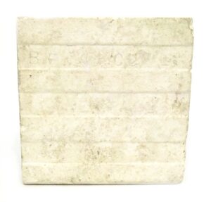 Square ceramic tile with a worn surface and minor age-related imperfections, shown as a close-up of one tile from a set of three.