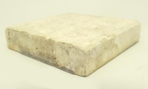 A close-up of a brown ceramic square tile with visible age-related imperfections and minor chips.