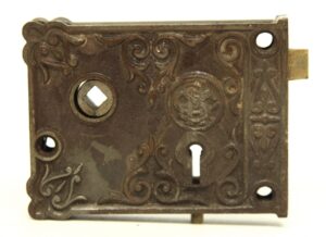 Ornate surface-mounted lock with decorative cast iron faceplate, keyhole, and latch bolt.