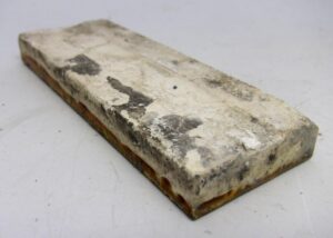 Ceramic tile with burnt brown edges and visible age-related chips and scrapes on the surface.