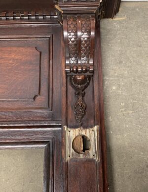 Close-up of a Rococo-style walnut fireplace mantel with carved details and a missing hardware opening, shown in dark wood tone reclaimed condition.