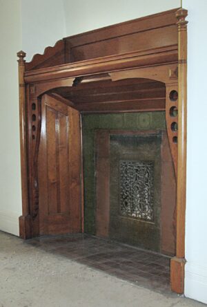 Traditional built-in mantel in a dark wood tone, shown in an alcove with geometric side detailing and an ornate firebox opening.