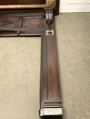 Oversize Rococo walnut fireplace mantel in dark wood tone, shown in a close-up of the corner with carved details and a visible opening for hardware, in reclaimed condition.