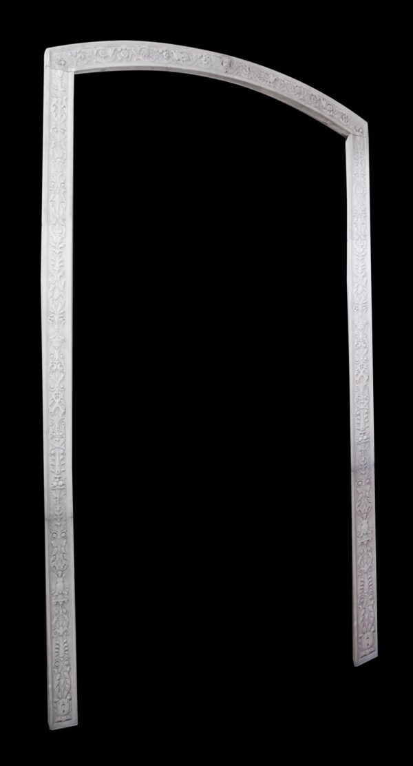 White carved marble arched molding with floral ornament on the vertical sides and curved top, shown as a tall door surround against a plain background.