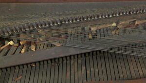 Close-up of an antique piano forte keyboard with strings and action components visible beneath the dark wood tone frame.