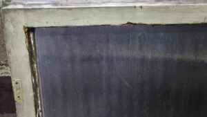 Close-up of a white wood-framed window with rippled glass and chipped paint along the edge.