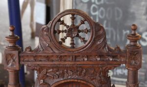 Close-up of a carved wooden chair back with a circular medallion and turned finials, showing the English Renaissance style in dark wood tone.