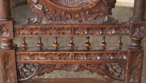 Close-up of a carved wooden chair showing detailed ornament on the back and stretcher with turned spindles below the seat.
