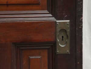 Close-up of a dark wood tone six-panel pocket door with a brass keyhole plate.