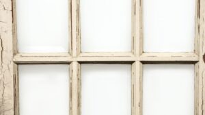 Antique French door with 15 beveled glass lites and a distressed white-painted wood frame, shown in close-up.