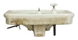 White porcelain sink with an integrated basin, side faucet openings, and visible wear, shown with a hairline crack near the back center.