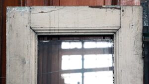 Close-up of the upper section of a wooden entry door with a narrow beveled glass panel and worn white paint.