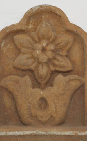 Floral terra cotta piece with a raised flower motif and arched top edge.