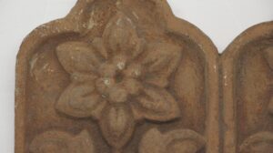 Close-up of a terra cotta floral piece with raised petal detail and a central raised dot, shown as part of a paired set.