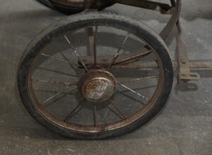 Close-up of a vintage baby stroller wheel with metal spokes and a rusted hub.