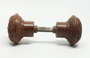 Pair of Victorian wood door knobs shown as a connected pair with a spindle, featuring concentric carved details and visible surface wear.