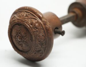 Victorian wood door knob with a concave center and carved floral scroll pattern, shown in close-up with the spindle partially visible.