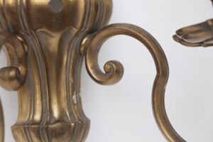 Close-up of an antique bronze wall sconce showing the decorative urn-shaped body and curled arm.