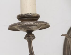 Close-up of a wall sconce with a slender arm, showing the distressed silver finish and candle cup detail.
