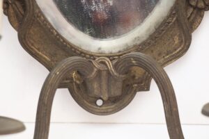 Close-up of an antique brass wall sconce with a beveled mirror inset and two curved arms.