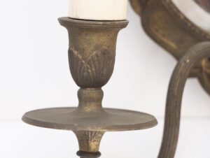 Close-up of an antique brass wall sconce arm and round candle plate with a white candle above.
