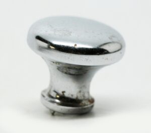 Chrome cabinet knob with a rounded top and short stem, shown in close-up with visible age wear and minor surface marks.
