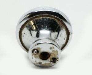 Chrome cabinet knob shown in close-up, with a rounded backplate and visible surface wear on the brass finish.