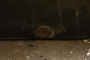Close-up of a black metal door panel showing a round eyeson lock near the bottom edge and worn surface details.