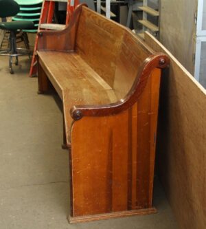 Extra long oak pew with a simple backrest and worn dark wood tone, shown from the front end at an angle.