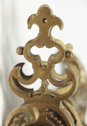 Close-up of an antique bronze French door handle back plate with a cutout scroll design and mounting hole.