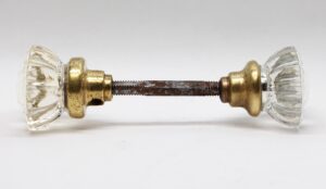 Pair of clear fluted glass door knobs with an antique brass shank and spindle, shown side by side.