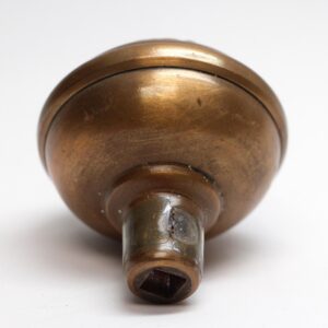 Antique brass passage door knob shown in close-up from the rear, with a rounded Victorian form and visible square spindle opening, plus surface wear from prior use.