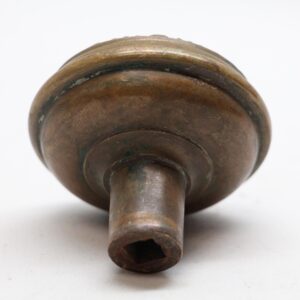 Antique bronze door knob shown in close-up from the back, with a cylindrical shaft and visible wear.