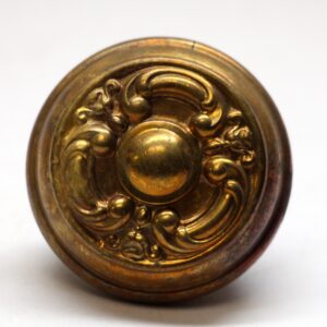 Close-up of an antique brass French door knob with an ornate circular rosette and worn surface finish.