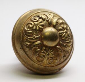 Close-up of an antique brass door knob with ornate Colonial floral embossing and a rounded center.