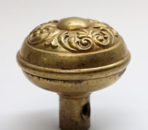 Close-up of an antique brass Colonial door knob with an ornate floral top and visible spindle hole.