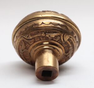 Close-up of an 1880s bronze door knob with a square spindle opening and engraved Vernacular pattern.