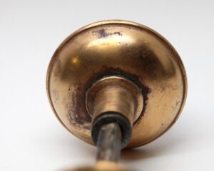 Close-up of a polished bronze door knob with a round backplate and spindle visible from the rear, showing worn patina and surface wear.