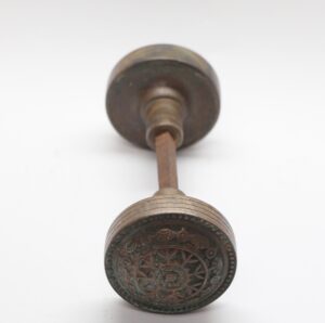 Antique bronze door knob with an ornate circular face and spindle shown in close-up.