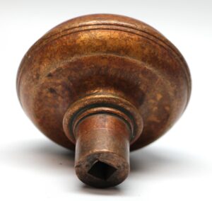 Antique bronze door knob with a concave center and square spindle opening, shown in close-up with a small dent in the middle.