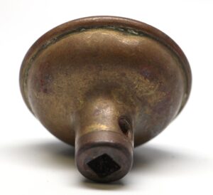 Antique brass door knob shown from the back, with a square spindle opening and concentric rounded form.