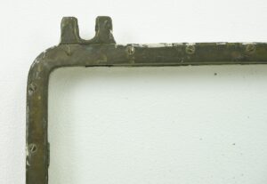 Close-up of a rectangular ship window with an antique brass frame, showing the top-left corner, mounting tabs, and screws with visible age wear.