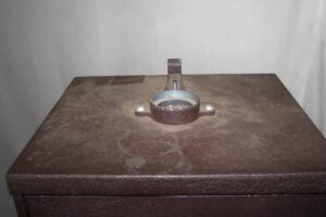 Close-up of a brown metal cabinet top with a central foot-press lever and circular latch hardware.