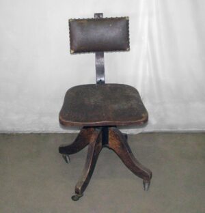 Antique rolling office chair with a dark wood tone oak seat, backrest, and curved base, shown front-facing with visible wear on the seat and back.