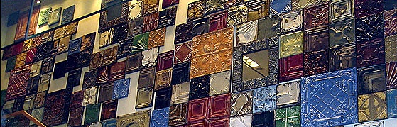 A wall decorated with a vibrant mosaic of colorful, embossed vintage-style metal tiles from Olde Good Things, each tile featuring unique shapes and intricate patterns.