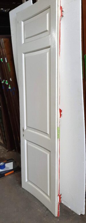 White wooden passage door with three recessed panels, shown at an angle with some hardware still attached.