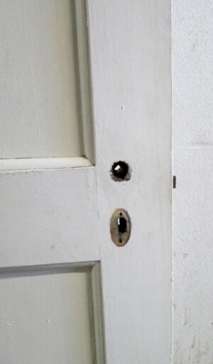 Close-up of a white wooden passage door showing the latch area and part of one of its three panels, with some original hardware still attached.