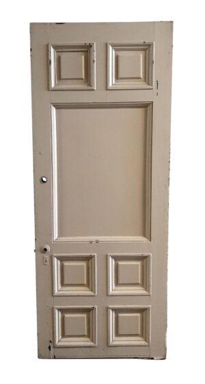 Tan wood entry door with six small raised panels and one large center panel, shown with a door knob hole and visible wear along the edges.