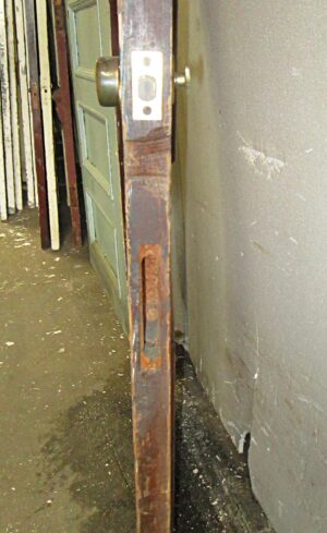Close-up of a dark wood tone wooden privacy door showing the edge, latch, and five-panel design, with a cracked piece of molding near the bottom.